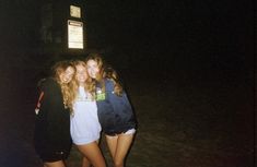 three girls standing next to each other in front of a street sign at night time