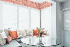 a glass table in front of a window with pillows on it and a vase filled with flowers