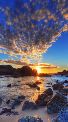 the sun is setting over some rocks on the beach with water and sky in the background