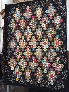 a large quilt hanging from the side of a building with many flowers on it's sides