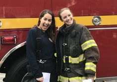 two women standing next to each other in front of a firetruck smiling for the camera