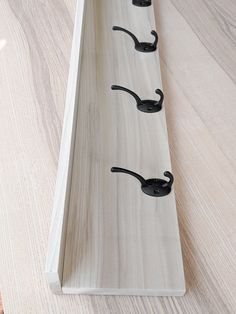 three black hooks are attached to the side of a wooden shelf on a wood floor