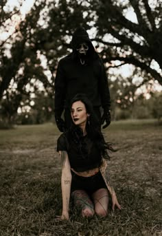 a woman sitting on the ground next to a man in a black hoodie and mask