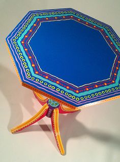 a blue and yellow table with an intricate design on the top, sitting on a white surface