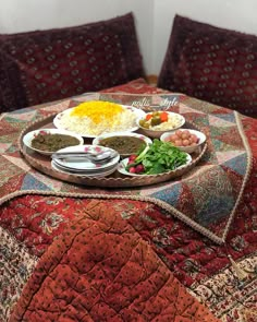 a table topped with plates of food on top of a colorful blanket covered table cloth