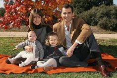 a man, woman and two children sitting on a blanket in the grass under a tree