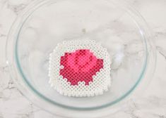 a cross - stitch heart in a glass bowl on a marble countertop with white and pink accents