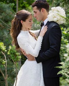 a bride and groom embracing each other in the woods