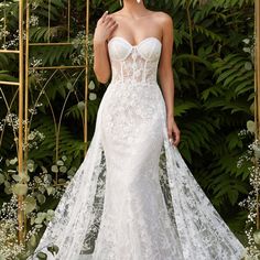 a woman in a white wedding dress standing next to a gold trellis and greenery