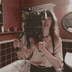 a woman holding up a camera in front of her face while standing next to a bathtub