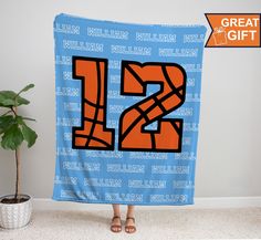 a person holding up a blue and orange towel with the number 12 printed on it