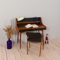 a desk with a chair, vase and book on it