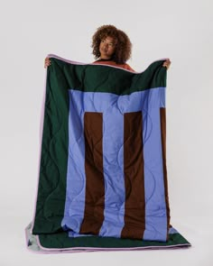 a woman is holding up a blanket with brown and blue strips on it in front of a white background