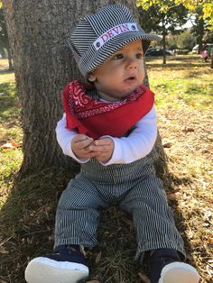 a little boy sitting under a tree wearing a hat and scarf