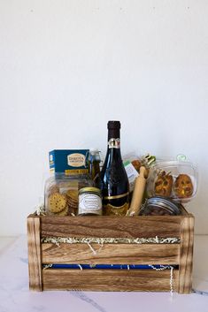 a wooden crate filled with assorted food and wine bottles next to a white wall