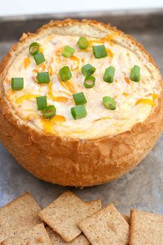 a baked dip in a bread bowl with crackers on the side and green onions