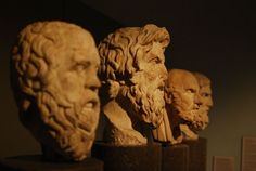 three statues of men with beards on display in a museum setting, one is looking at the camera