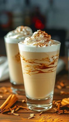 two glasses filled with dessert sitting on top of a wooden table next to cinnamon sticks