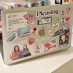 an open laptop computer sitting on top of a white desk covered in stickers and magnets