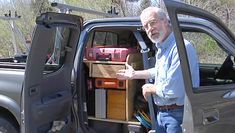 an older man standing in the back of a truck with its doors open and lots of items inside