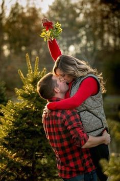 a man and woman are kissing in front of a christmas tree at the same time