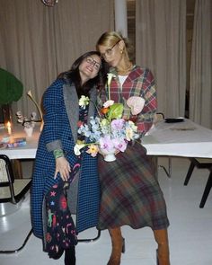 two women standing next to each other in front of a table with flowers on it