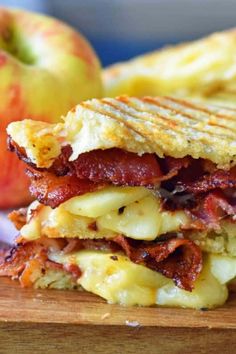 a bacon, cheese and apple sandwich on a cutting board with an apple in the background