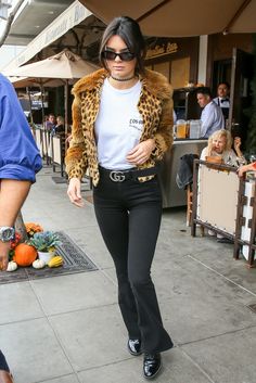 a woman walking down the street wearing black pants and leopard print jacket with her hands in her pockets