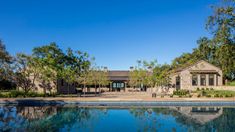 a large pool in front of a house with trees and bushes around it, next to the swimming pool