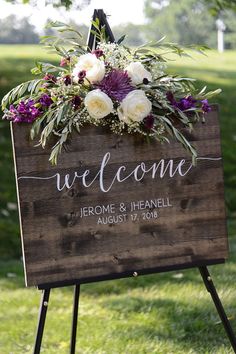 a welcome sign with flowers and greenery on it in front of a grassy field