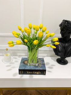 a vase filled with yellow tulips sitting on top of a table next to a statue