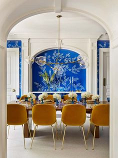 a dining room with blue and white wallpaper, yellow chairs and a chandelier