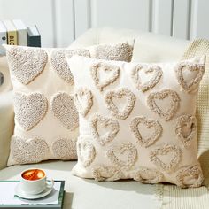 two pillows with hearts on them and a cup of coffee next to each other sitting on a couch