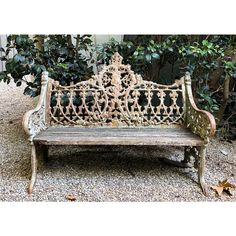 an old wooden bench sitting in the middle of a gravel area next to some bushes