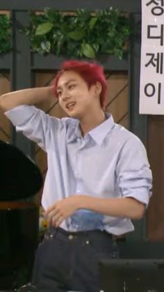 a man with red hair standing next to a piano and holding his hand on his head