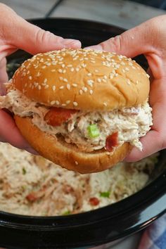 someone is holding a chicken salad sandwich over a bowl of coleslaw and slaw