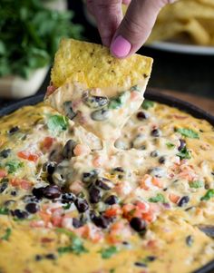 a hand dipping a tortilla chip into a black bean and cheese dip