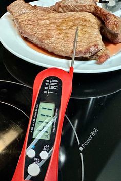 a meat thermometer sitting on top of a stove next to some steaks