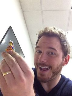 a man holding up a toy figurine in his right hand and smiling at the camera