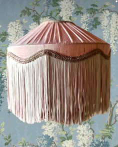 a pink lamp shade with fringes hanging from it's sides on a floral wallpapered wall