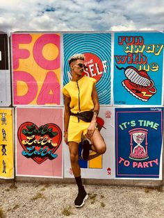 a woman standing in front of a wall with posters on it and her legs crossed