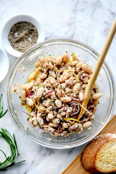 a glass bowl filled with beans and bread on top of a marble counter next to some herbs