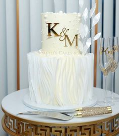 a wedding cake with the initials k and m sitting on a table next to two wine glasses