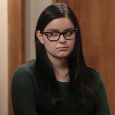 a woman wearing glasses sitting down in front of a door