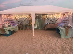 a tent set up on the beach for an outdoor party with lights strung from it