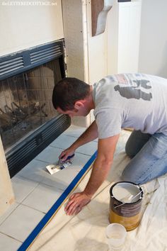 a man is painting the floor in front of a fire place with blue tape and a brush