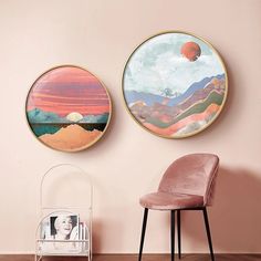 two round paintings on the wall next to a pink chair in a room with wooden floors