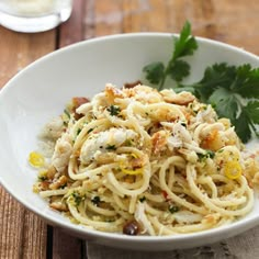 a white bowl filled with pasta and garnished with parsley next to a glass of water