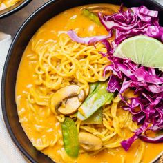 two bowls filled with noodles and vegetables on top of a table