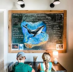 two children sitting at a table in front of a chalkboard with writing on it